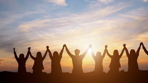 Eight people silhouetted against a sunset stand in a row with joined hands raised high