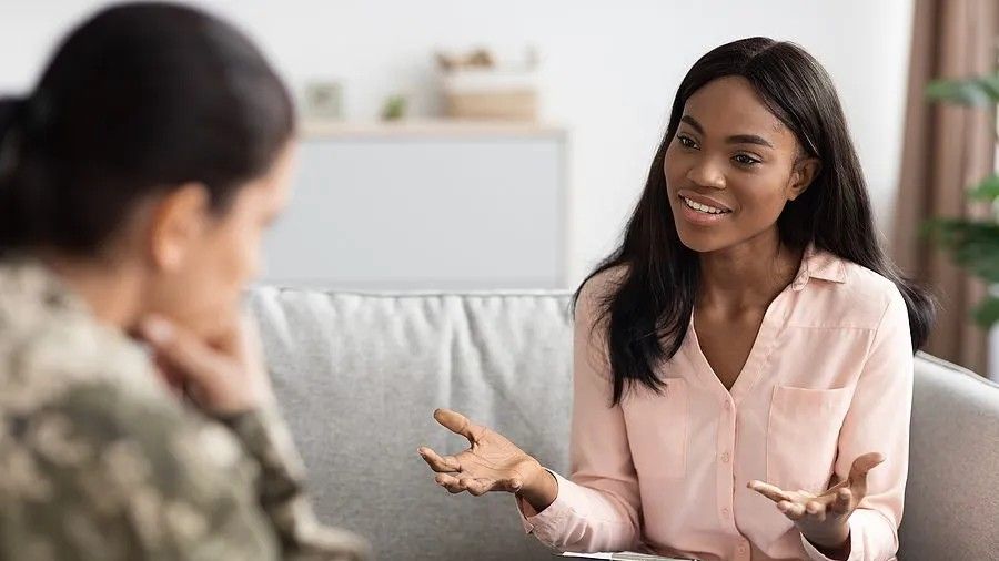 A counselor gestures as she speaks with a person in military uniform seated across from her