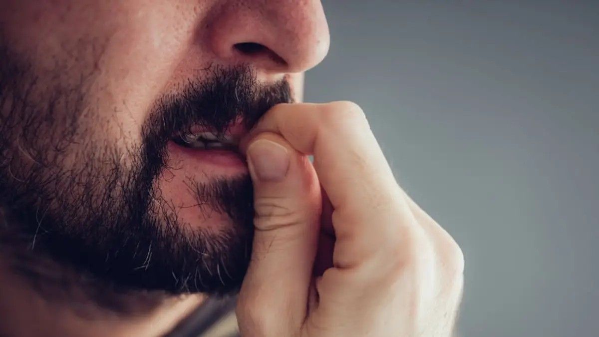 Close-up of a bearded man biting his fingernail against a plain grey background