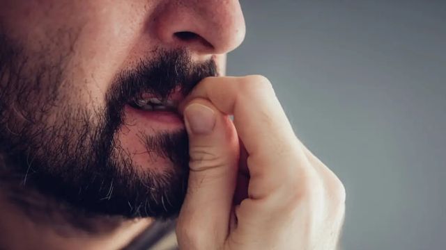Close-up of a bearded man biting his fingernail against a plain grey background