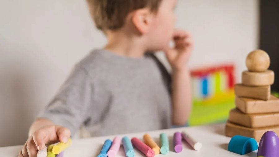 A young boy at a table lining up colorful chalk sticks in a neat row beside wooden toys