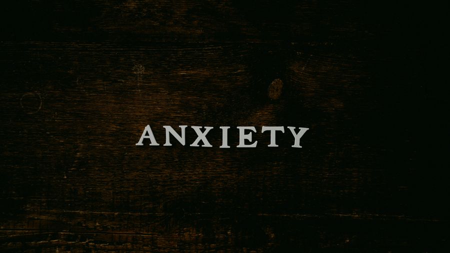 The word "ANXIETY" spelled in white block letters on a dark, weathered wooden surface
