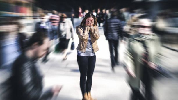A woman stands still with her hands over her face as a blurred crowd rushes past