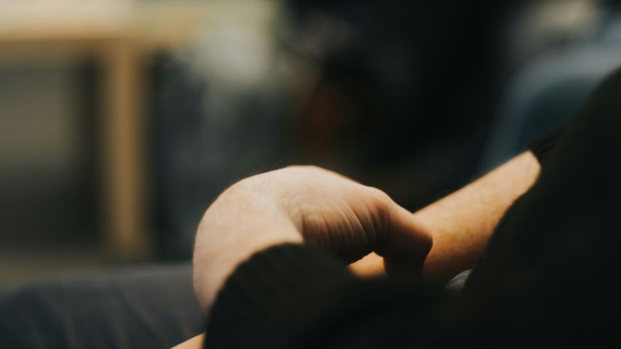 Close-up of a person's hands resting loosely in their lap in a warm, dimly lit room